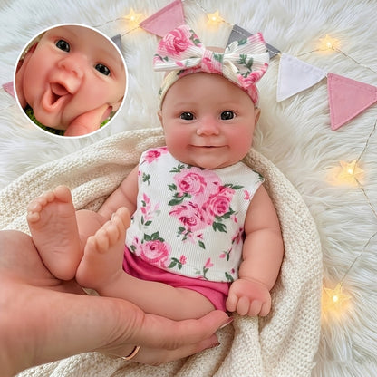 Bambola reborn Maddie in silicone estensibile da 30 cm con sorriso vestita con abitino floreale rosa