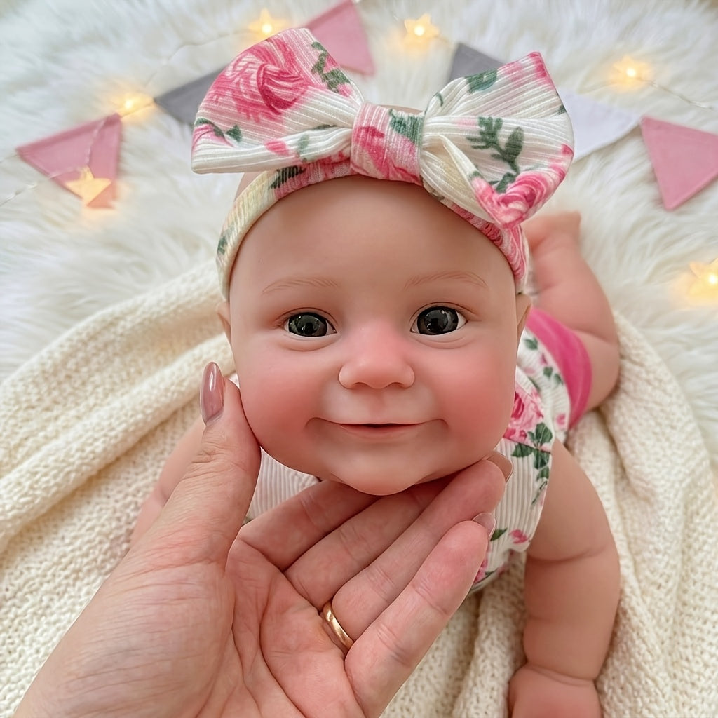 Bambola reborn Maddie in silicone estensibile da 30 cm con sorriso vestita con abitino floreale rosa