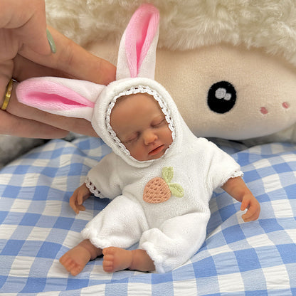 Bambola reborn Loulou Mini in silicone da 15 cm con pelle scura vestita da coniglio bianco