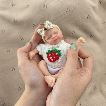 Bambola reborn Pascale in silicone da 15 cm con occhi chiusi e maglione bianco a fragole