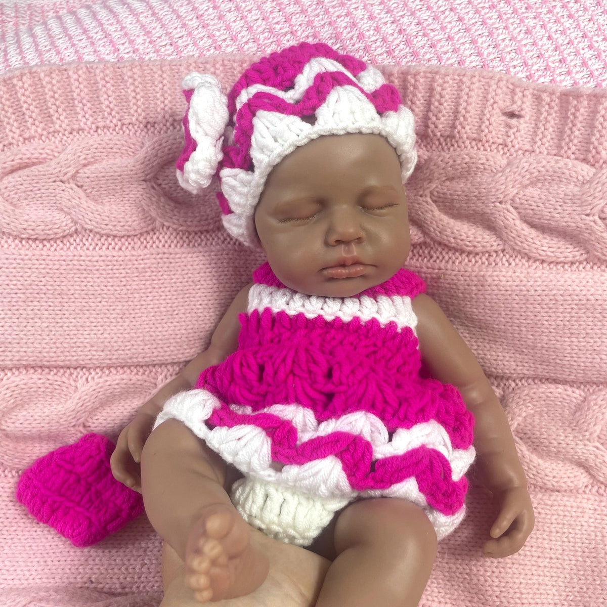 Bambola reborn Loulou in silicone 30cm realistica con pelle scura vestita con un maglione mentre dorme