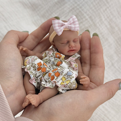 Bambola reborn Loulou Mini in silicone da 15 cm con pelle scura e vestiti floreali