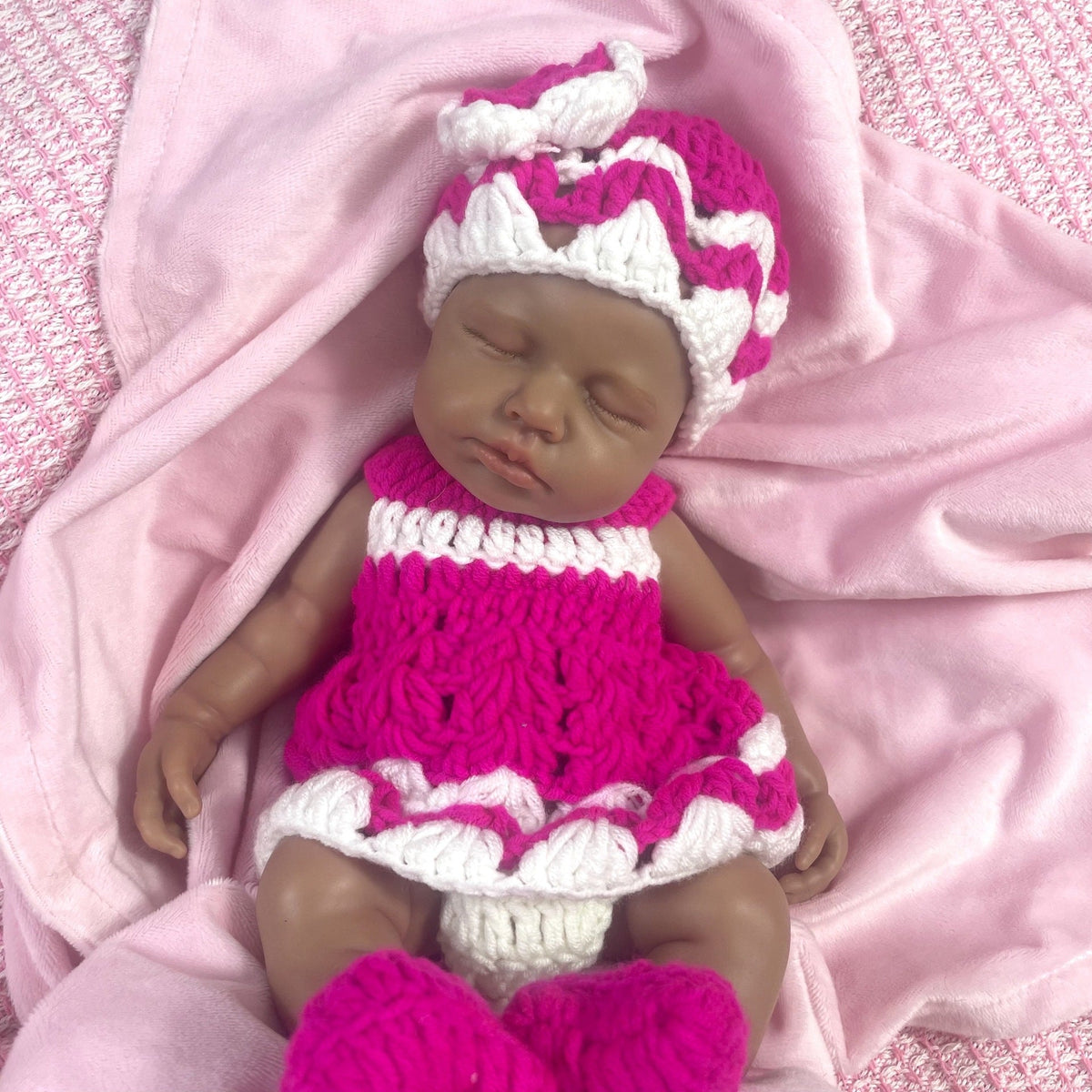 Bambola reborn Loulou in silicone 30cm realistica con pelle scura vestita con un maglione mentre dorme