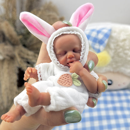 Bambola reborn Loulou Mini in silicone da 15 cm con pelle scura vestita da coniglio bianco